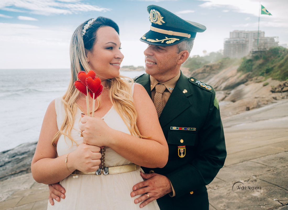 fotos de ensaio pre casamento, noiva abraçada pelo noivo por trás e segurando uns corações no forte de copacabana por andré nogueira fotografia