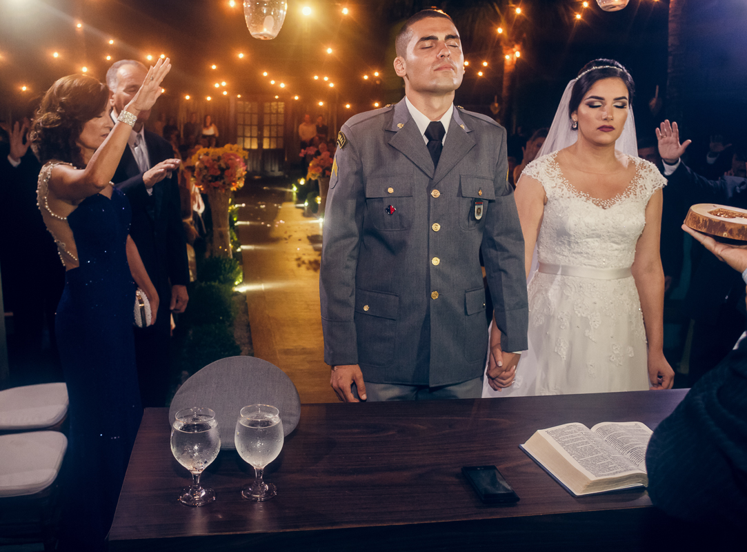 noivos de olhos fechado e sendo abençoado pelos pais e convidados