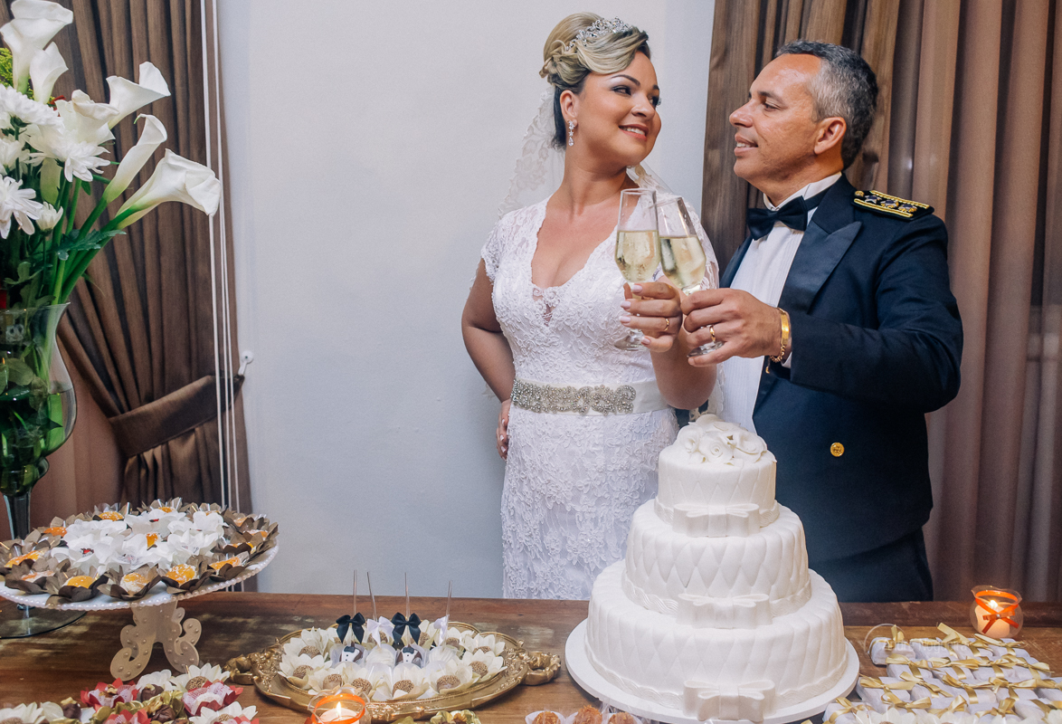atrás da mesa do bolo no salão de festas do forte de copacabana, os noivos brindam seu lindo casamento