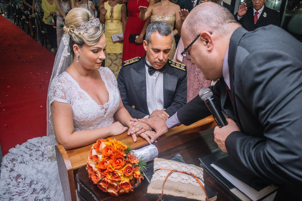 pastor coloca a mão sobre as mãos do casal que estão ajoelhados, para abençoar a alianças deles