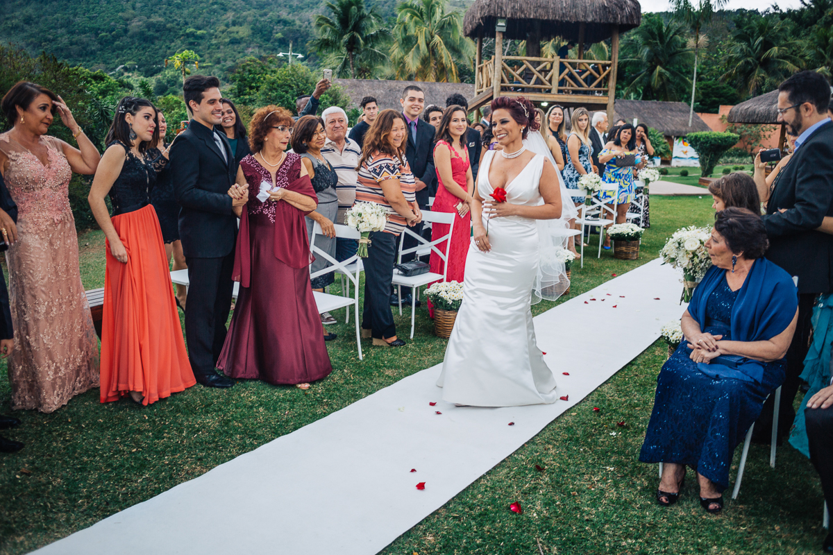 noiva entrando pelo corredor do lugar de cerimônia da chácara do sapê segurando uma rosa vermelha, rumo ao altar para o seu casamento