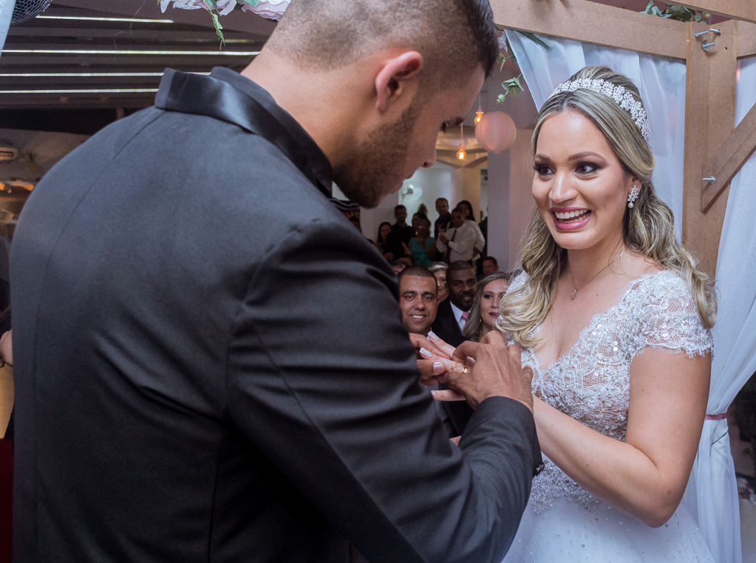 fotografia de casamento rj, noivo coloca aliança nos dedos da noiva, que observa toda feliz, cerimônia batuli festas nova iguaçu, foto por andré nogueira fotografia