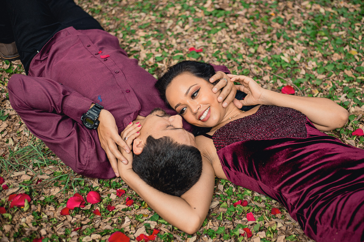 casal de noivos deitados no gramado olhando um para o outro cheio de pétalas de rosas em volta do casal