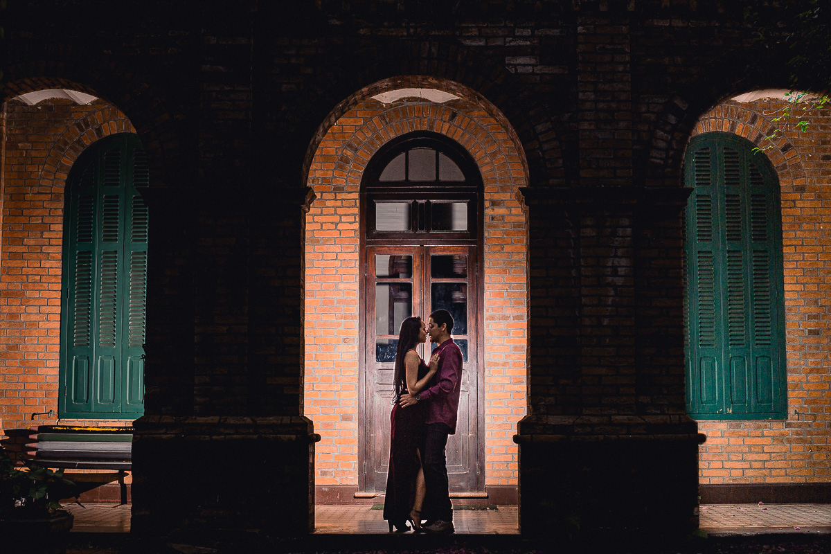 casal de noivos vestidos de rupa marsala se abrasando de frente de um casarão antigo