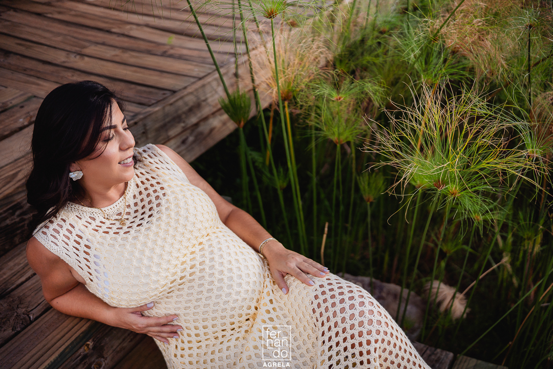 fotografia de ensaio gestante de mulher gravida apoiada em uma escada com plantas de papiro ao fundo
