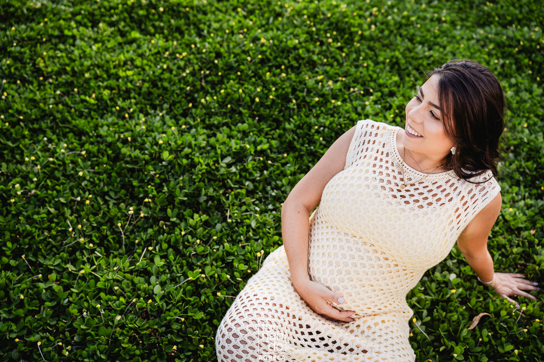 foto de ensaio de gestante sentada em um jardim de pequenas plantas verdes