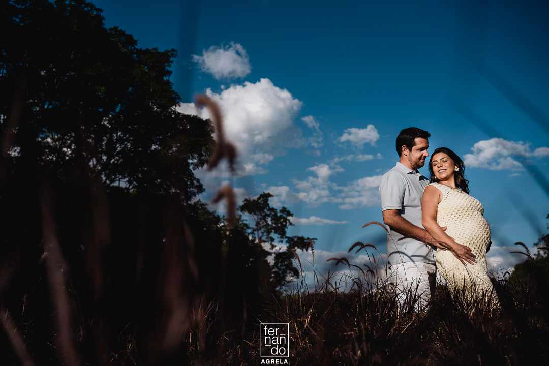 foto de casal com ceu azul ao fundo e vegetação em primeiro plano, o casal esta junto e a mulher esta gravida