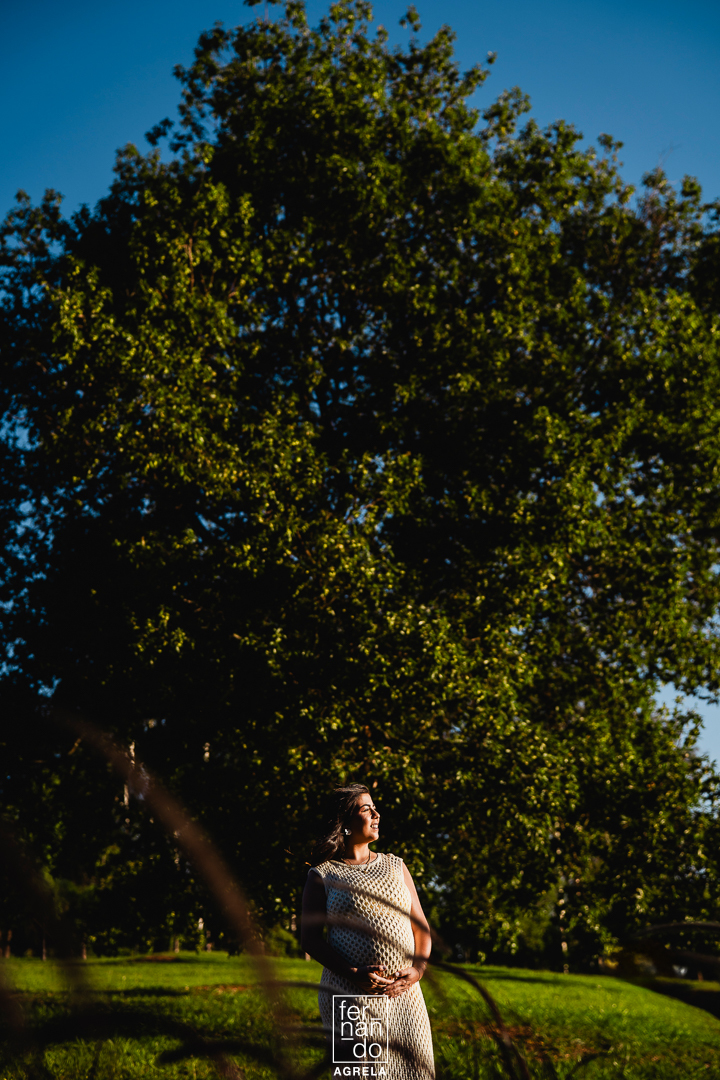 ensaio de mulher gestante com arvore grande ao fundo e ceu azul