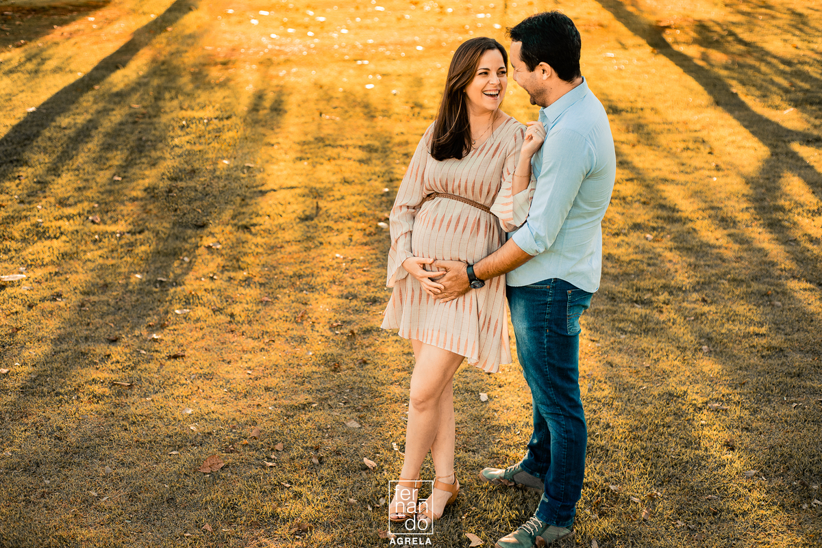 mae sorrindo durante a gestação em foto junto com o pai no fim detarde com sol ao fndo