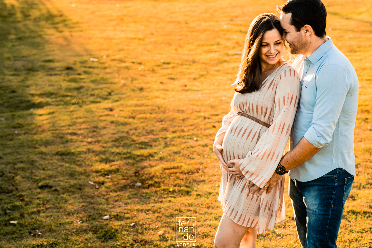 ensaio com pai e mae gestantes no fim de tarde com gramado ao fundo