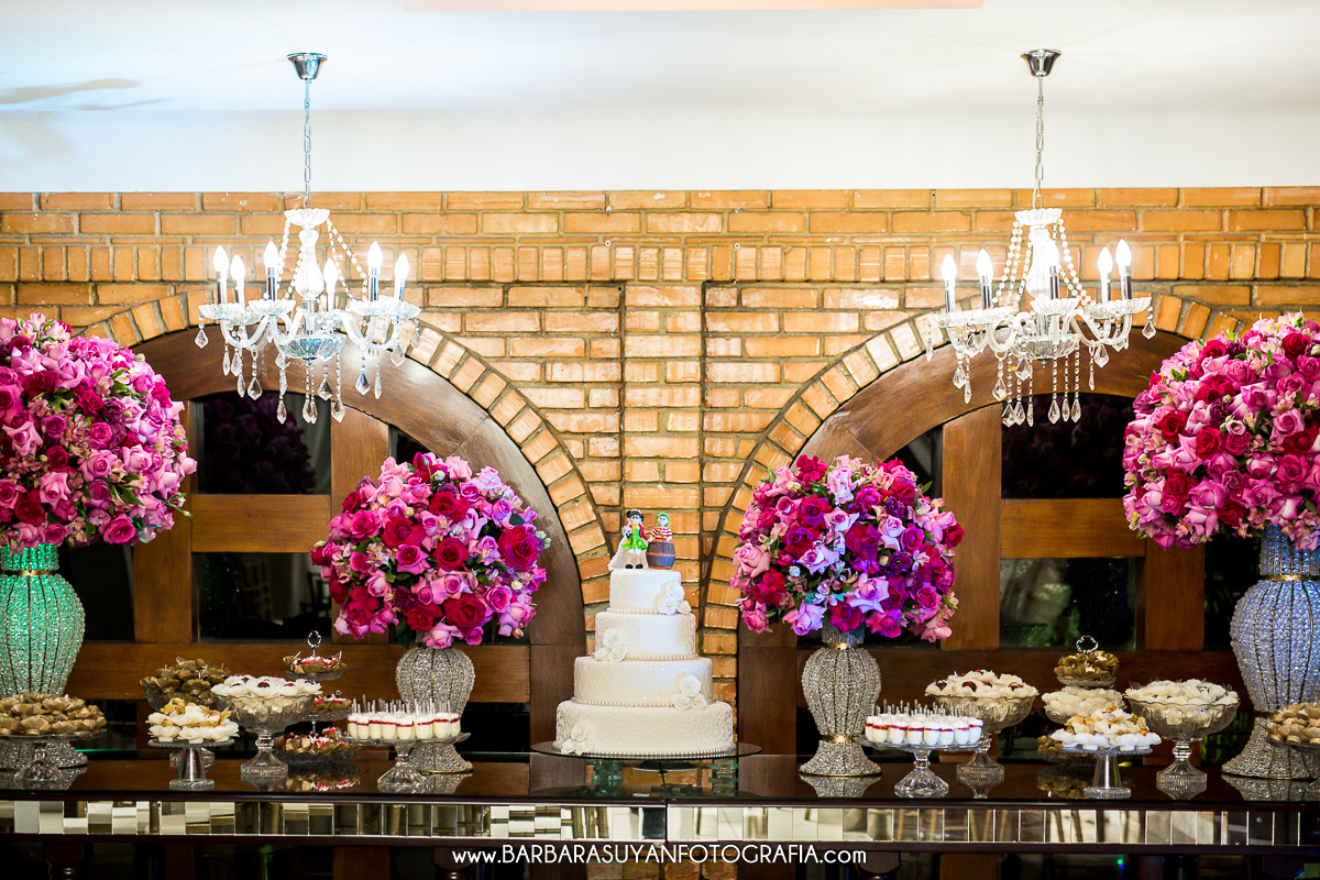 Bolo de casamento branco do casamento de Lívia e Thiago no Chalé Pampulha. Topo do bolo em biscuit bonecos chiquinha e chaves. Decoração com flores naturais rosas