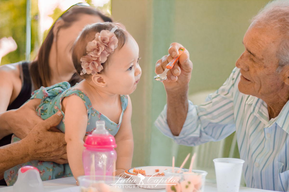 Neta sendo alimentada pelo avô, na sua festa em comemoração ao seu primeiro ano de vida