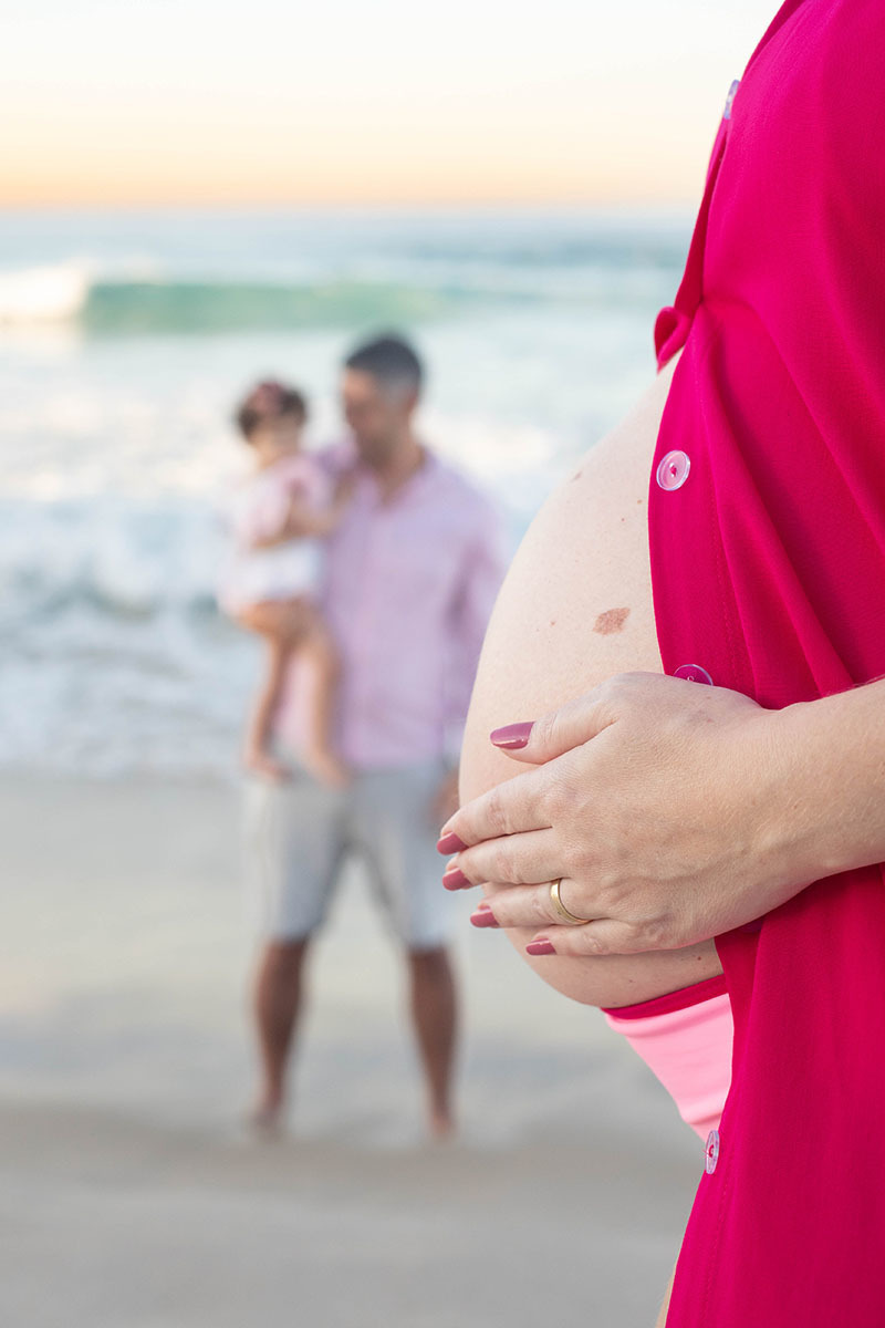 Detalhe das mãos sobre a barriga em ensaio gestante na praia carioca