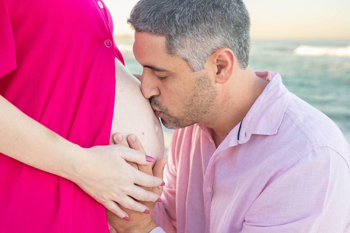 Beijo na barriga entre as ondas da Praia da Barra em ensaio gestante
