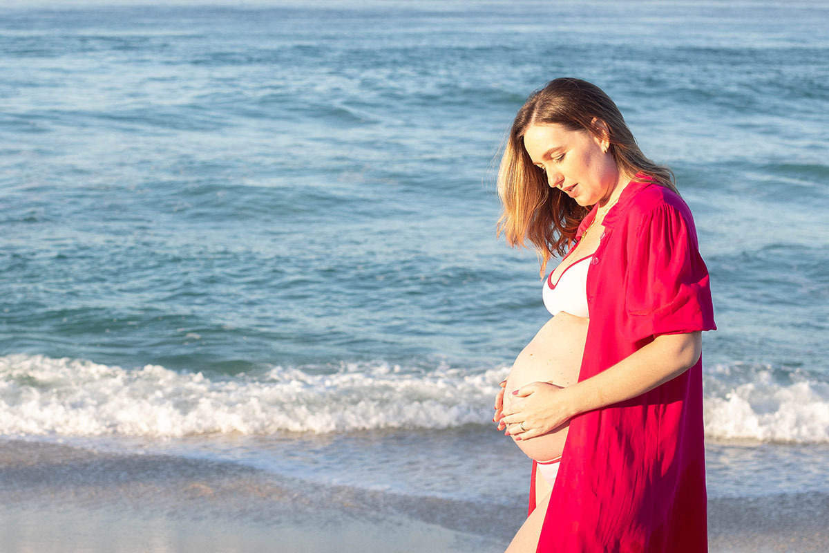 gestante com a mão na barriga em ensaio na praia da Barra no RIO