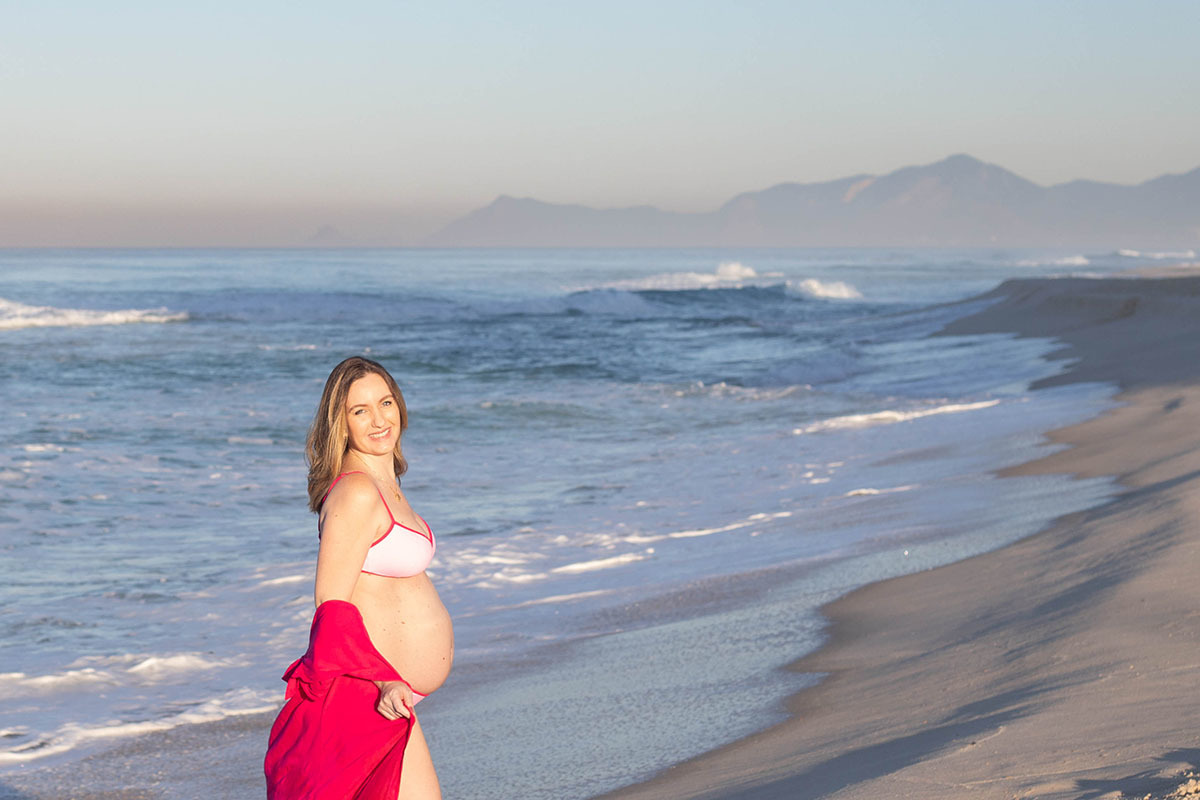 Gestante na areia com olhar tranquilo no ensaio na praia