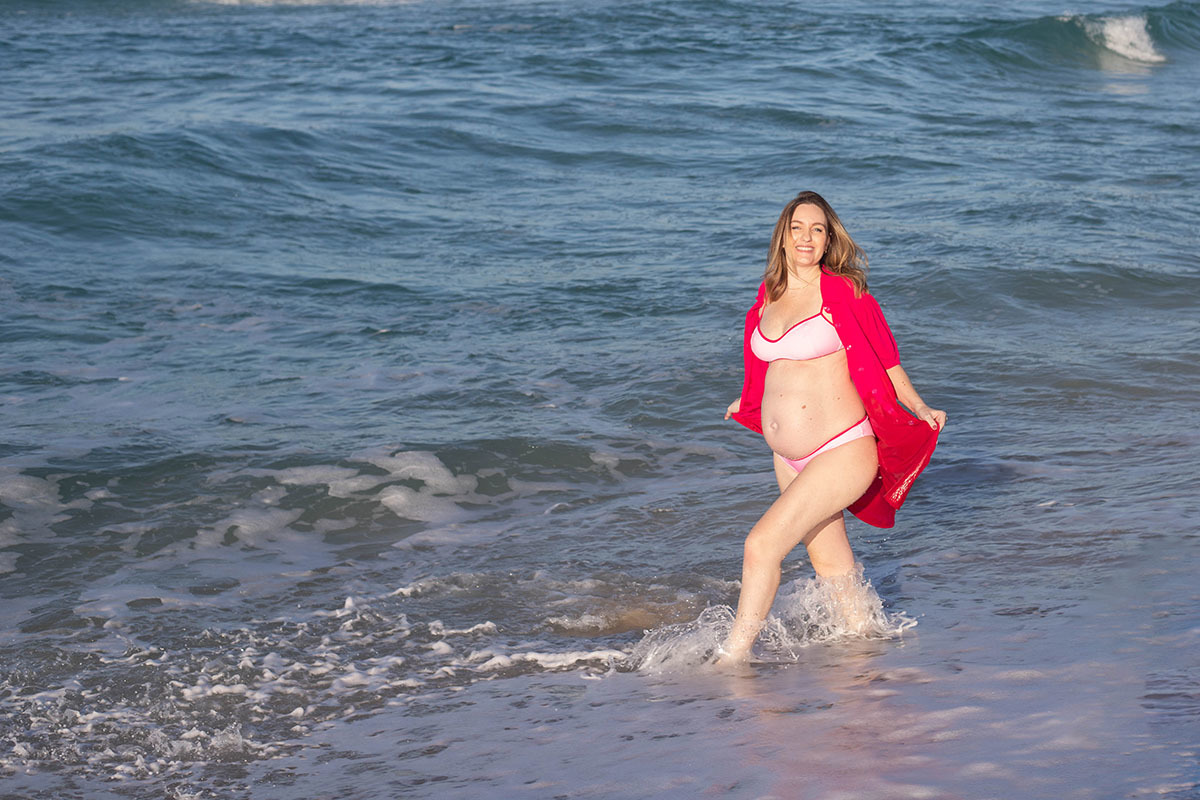 Gestante na orla da Barra usando vestido rosa vibrante em ensaio fotográfico