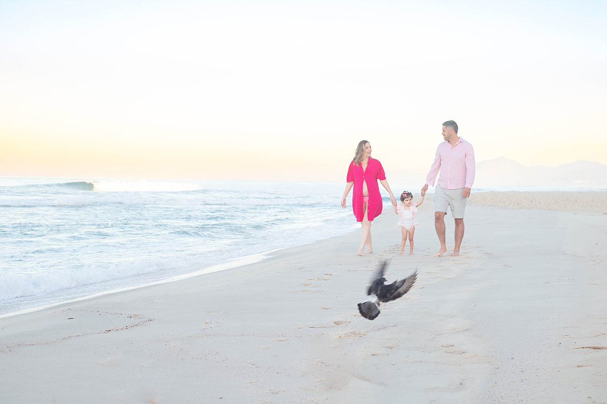 casal de mãos dadas com a filha à beira-mar, em ensaio na Barra do RJ