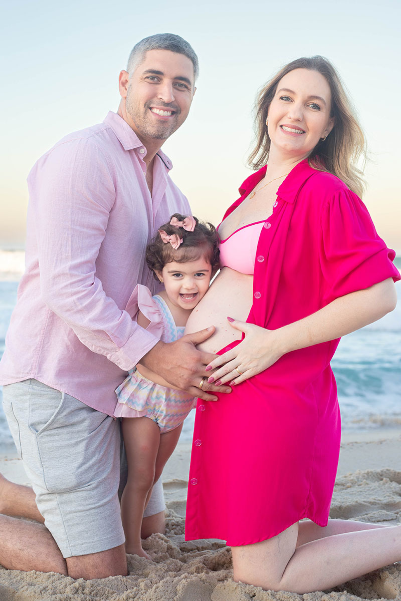 Detalhe da filha abraçando a mãe grávida em ensaio de família na praia