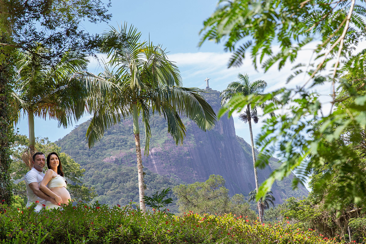 Casal  em ensaio gestante no Jardim Botânico, cercada por flores e verde.e o Corcovado ao fundo.