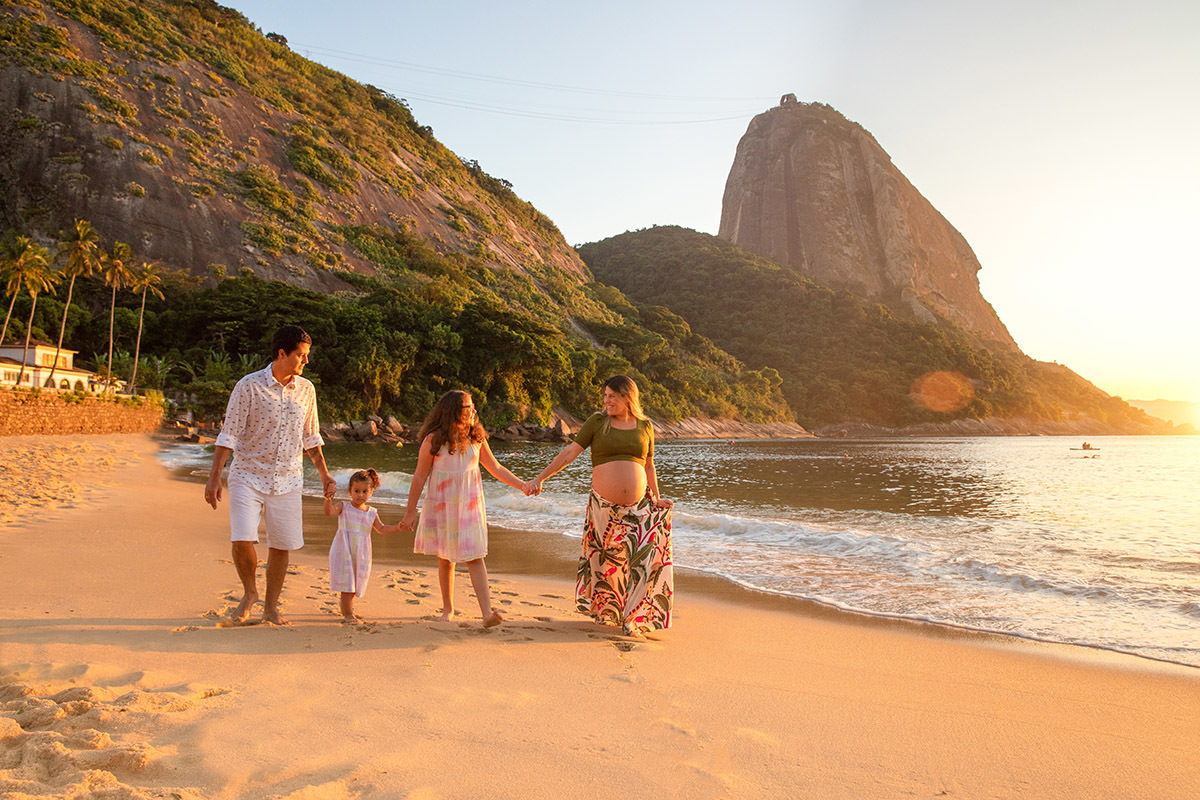 gestante, marido e duas filhas, andando de mãos dadas na areia da Praia Vermelha ao nascer do sol - ensaio gestante - nascer do sol - Rio de Janeiro - RJ.
