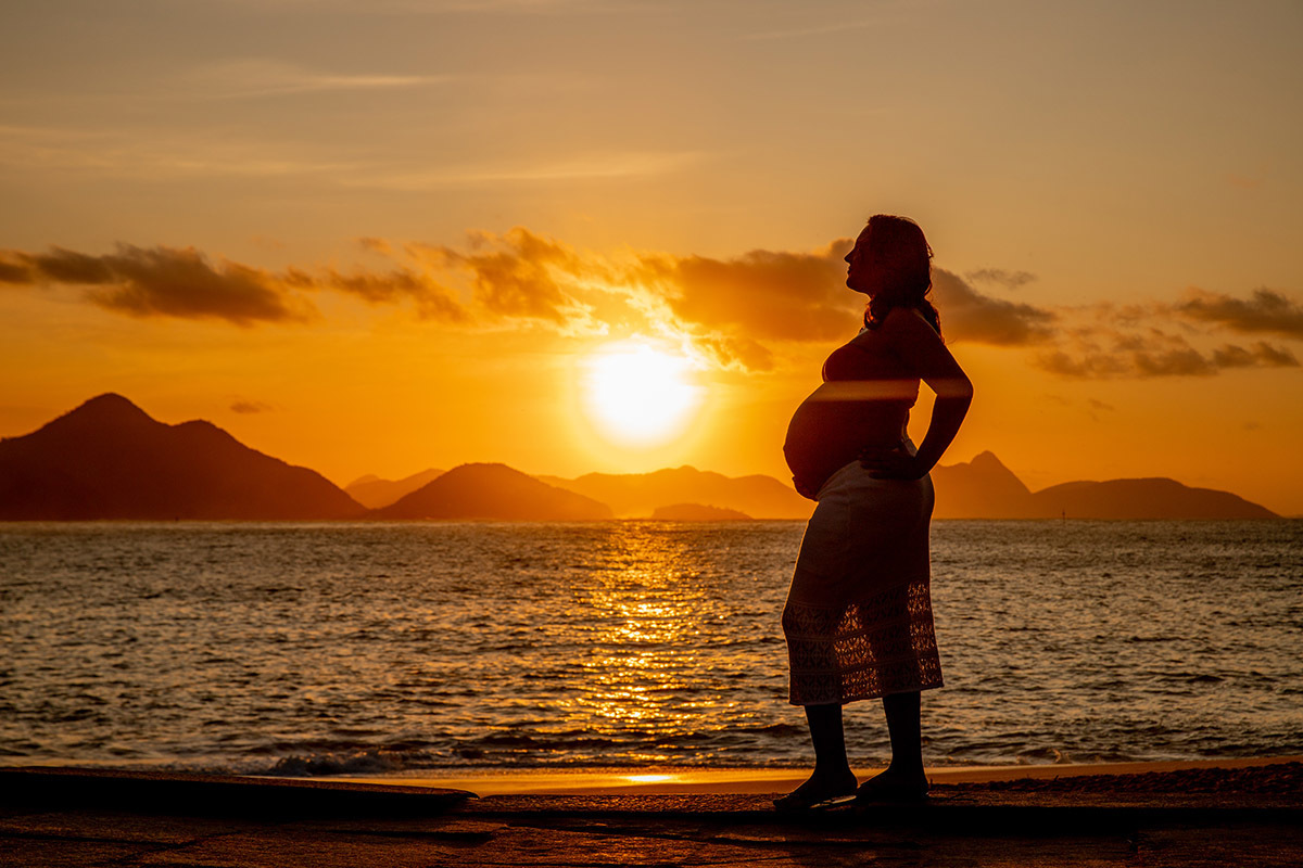 Silhueta de Gestante na Praia Vermelha com o sol dourado iluminando o ensaio.