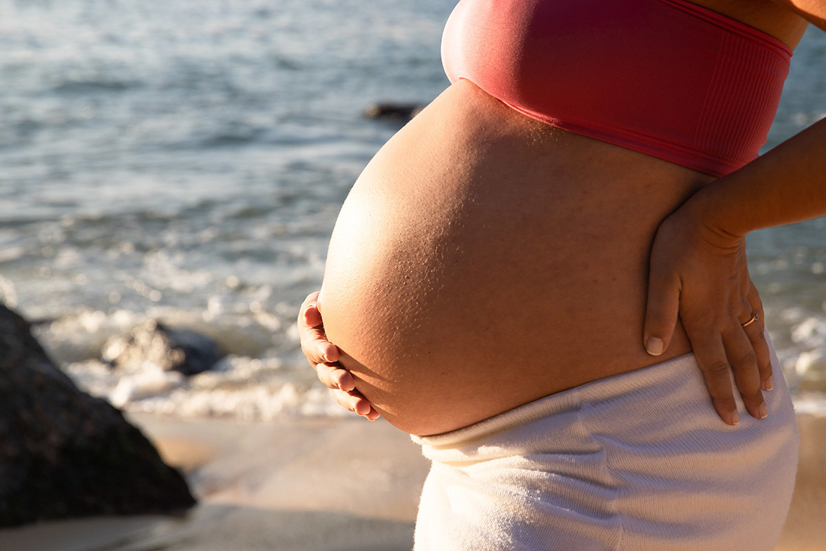 Detalhe da barriga da gestante iluminada pela luz do entardecer na Praia Vermelha.