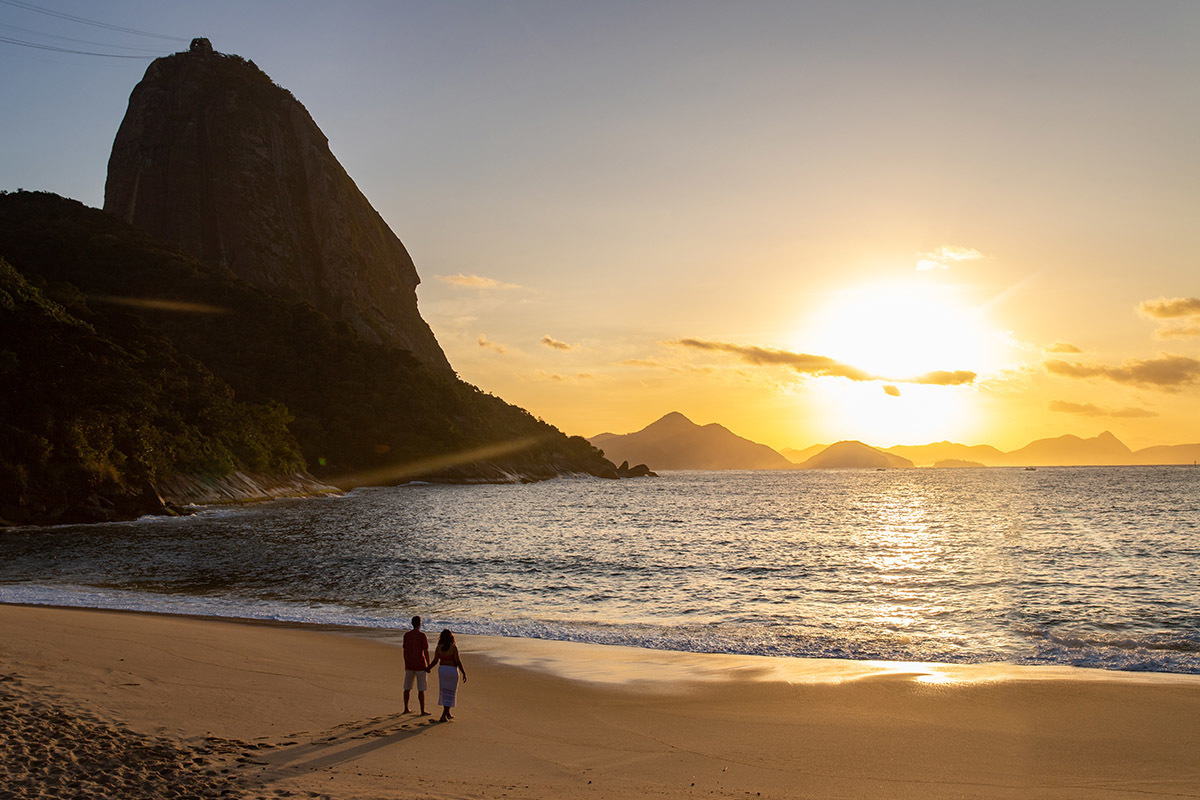 Casal na Praia Vermelha com o sol nascendo ao fundo, atrás do Pão de Açúcar