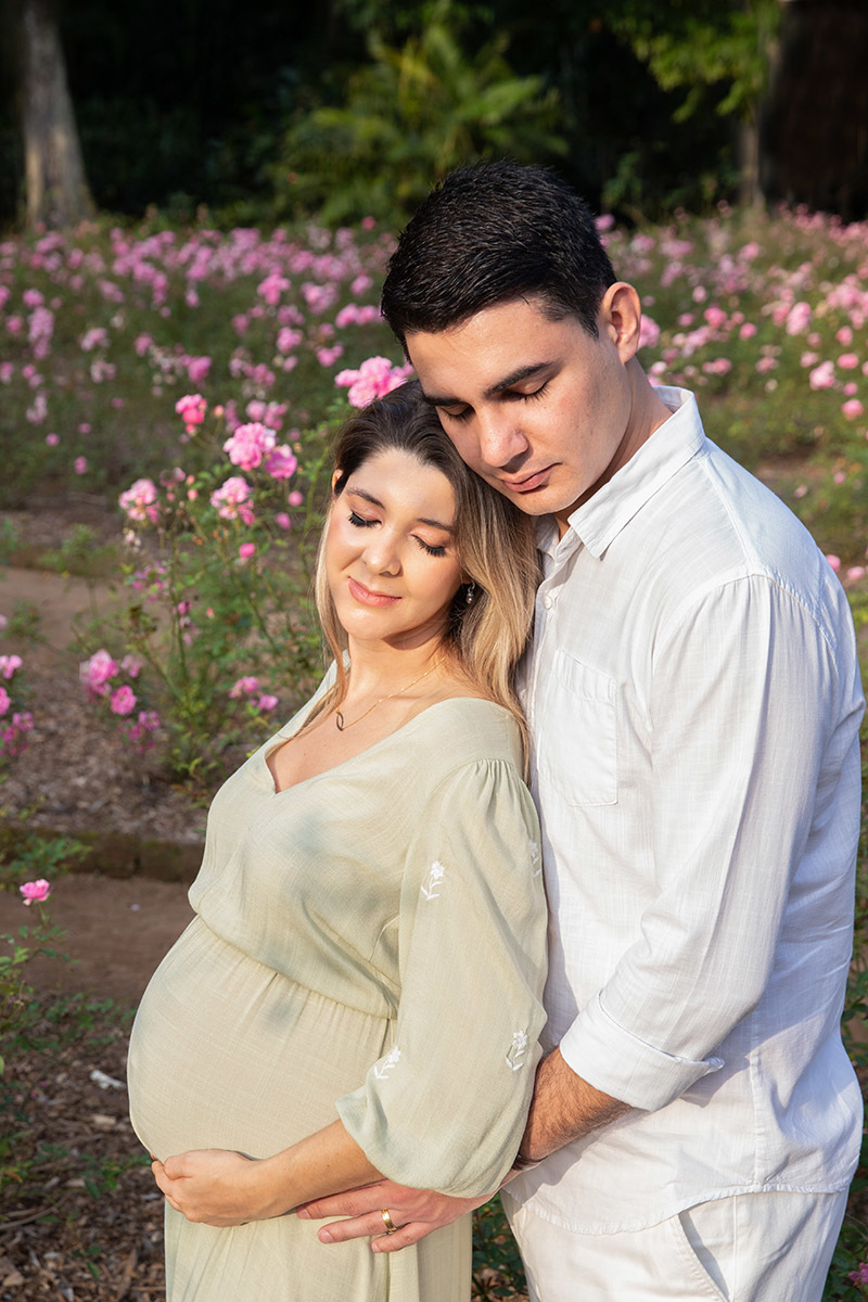 Casal em ensaio de gestante no Jardim Botânico, cercados por flores.