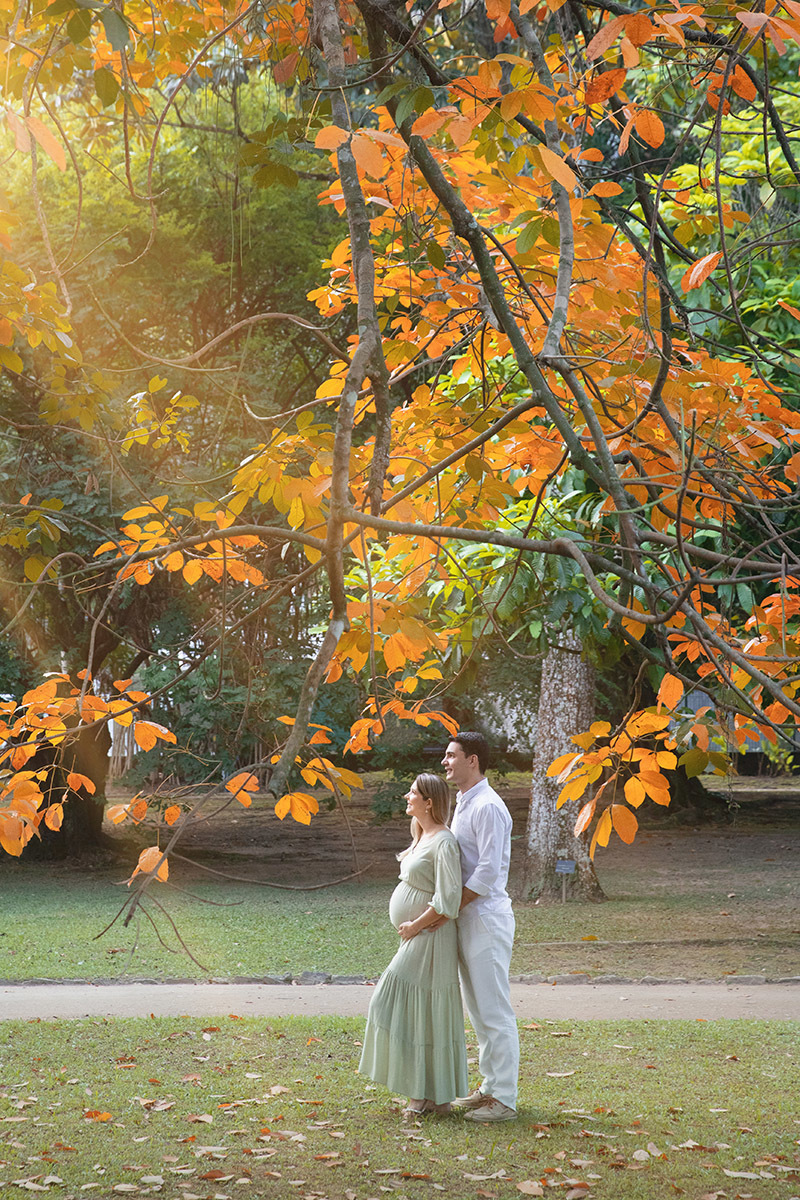 Ensaio de gestação ao ar livre com cenário natural de folhas alaranjadas no Jardim Botânico do Rio.