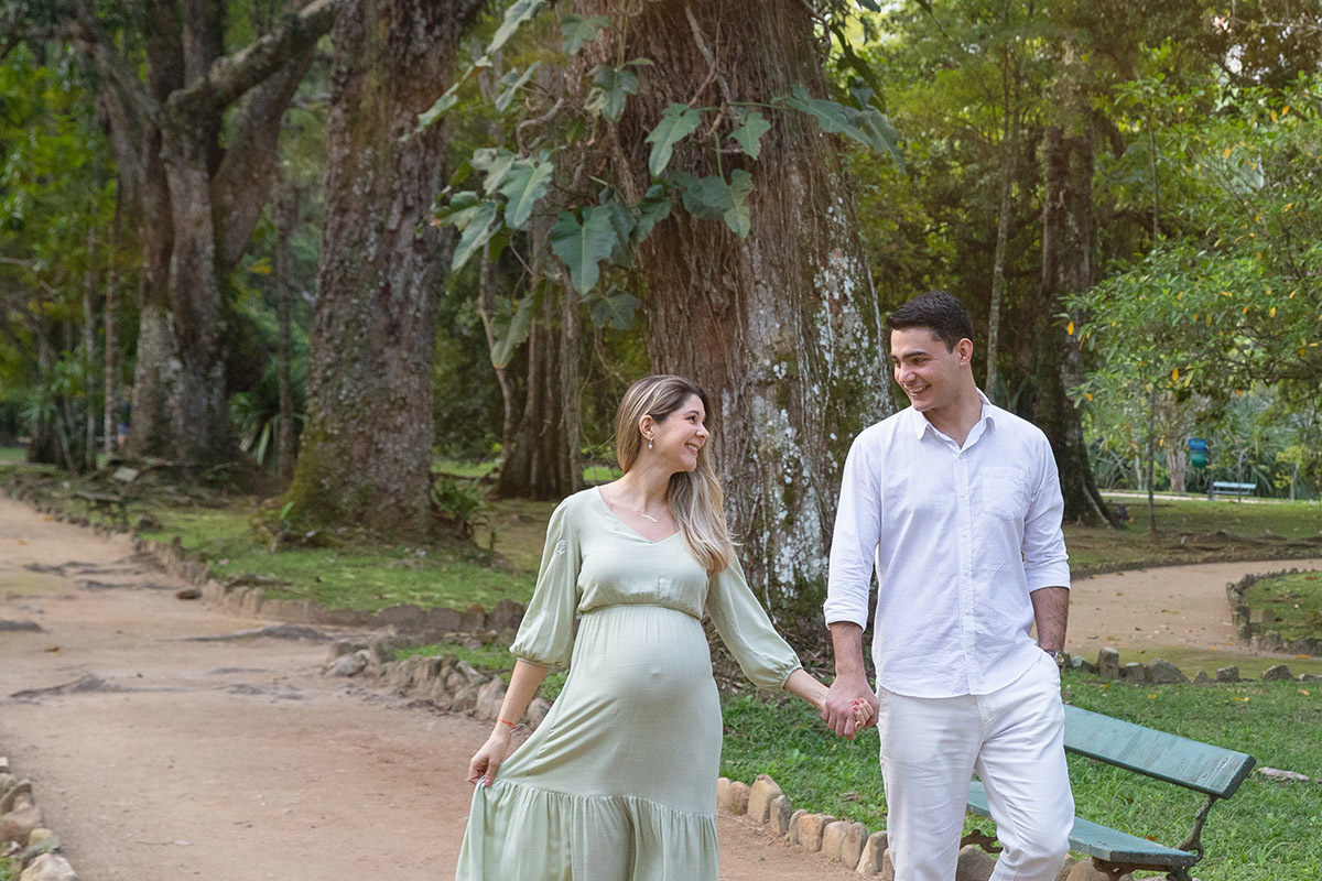 Ensaio de gestante ao ar livre, casal caminhando por alameda de árvores no Jardim Botânico do Rio.