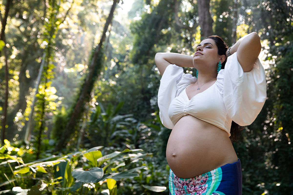 Foto de gestante sorrindo no Parque Lage, luz natural entre as árvores do Rio.