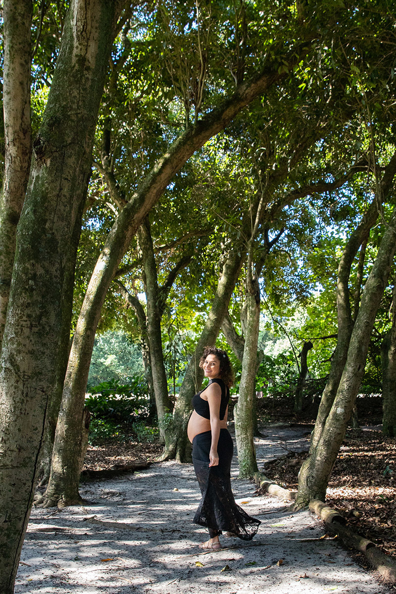 Foto artística da gestante entre raízes e luz suave do bosque carioca