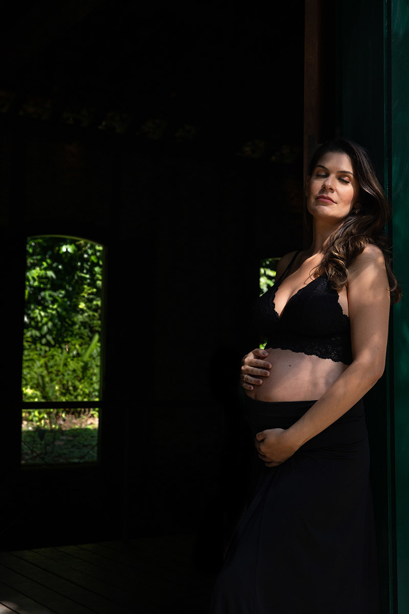 Gestante em ensaio no Jardim Botânico RJ, exibindo a barriga em pose carinhosa.