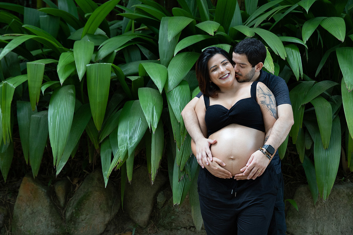 Casal se abraçando em ensaio gestante com folhagens ao fundo no Jardim Botânico.