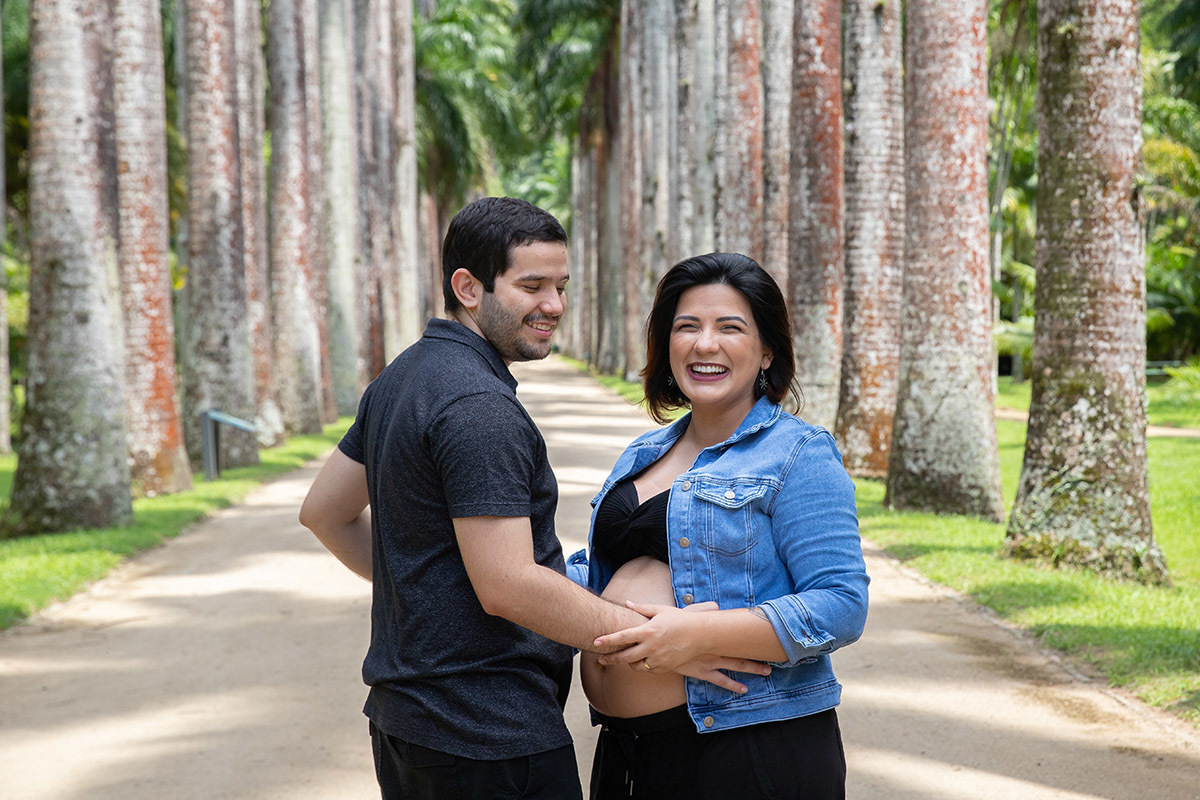 Casal sorrindo em ensaio gestante entre as árvores do Jardim Botânico.