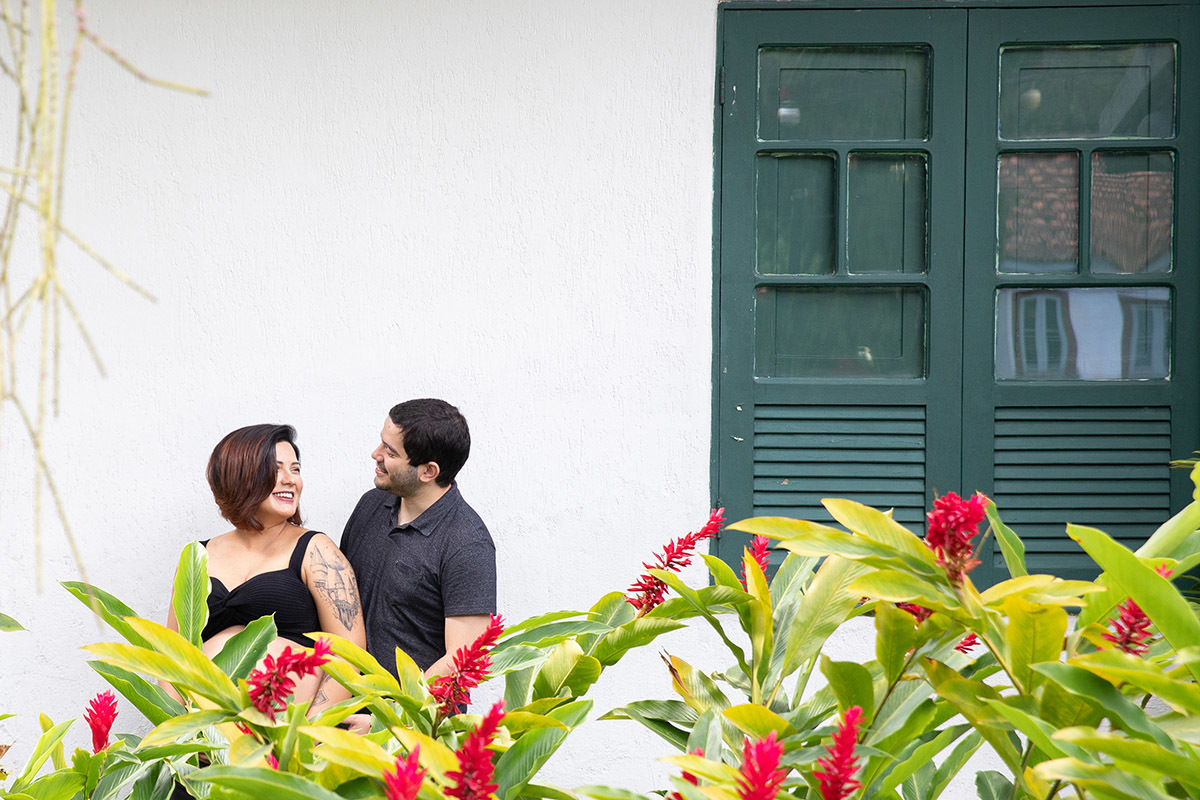 Casal sorrindo em meio às flores vermelhas no Jardim Botânico.