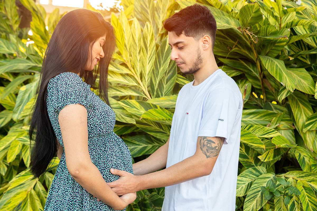 Casal em ensaio de gestante com luz natural entre as árvores.