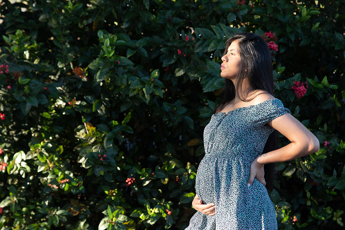 Foto de gestante sorrindo em ensaio cercada de folhas verdes.