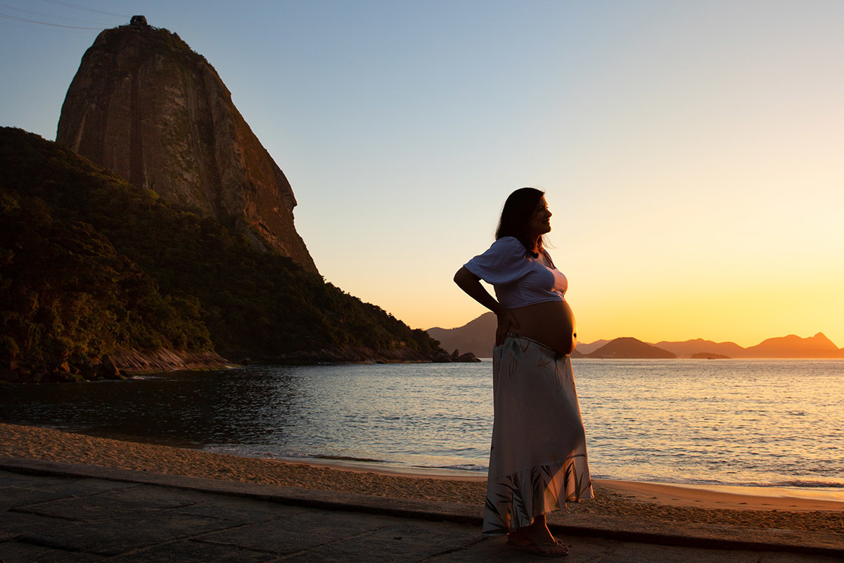 Foto de gestante na Praia Vermelha, com vista para o Pão de Açúcar no Rio de Janeiro.