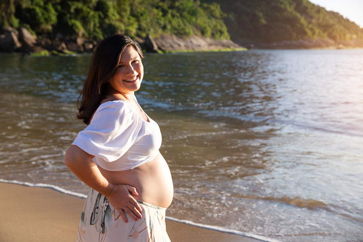 Foto de gestante sorrindo na Praia Vermelha, ensaio ao ar livre no Rio de Janeiro.