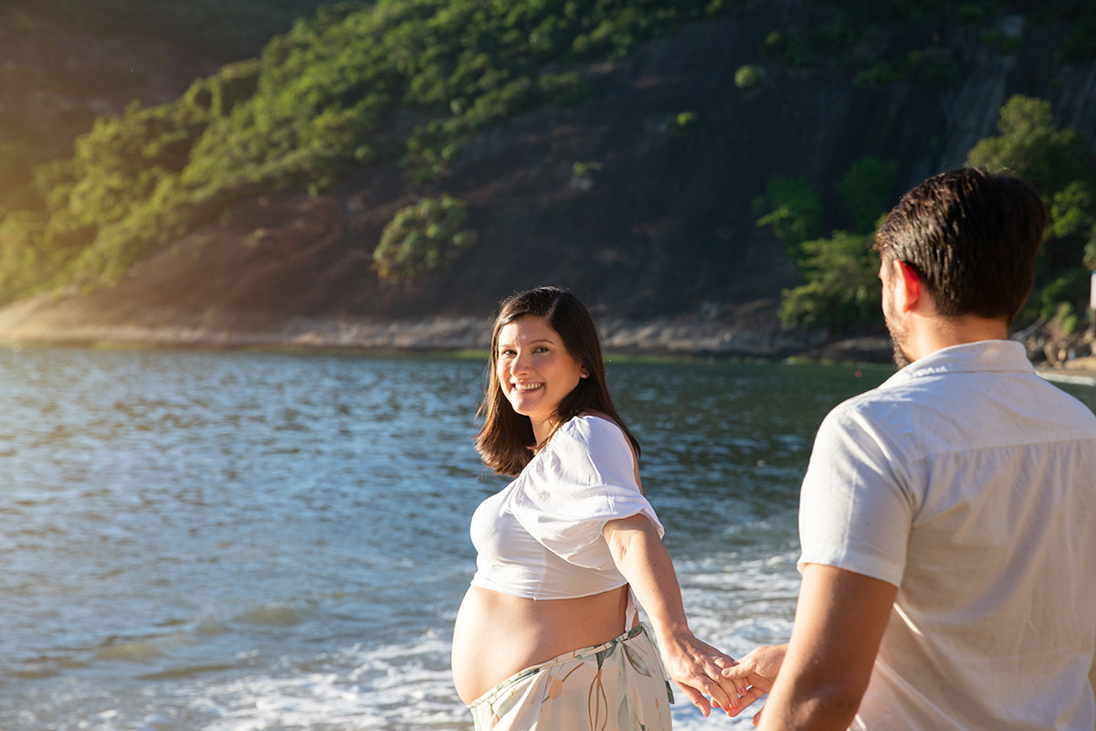 Gestante em ensaio na Praia Vermelha, com o mar azul como cenário de fundo.