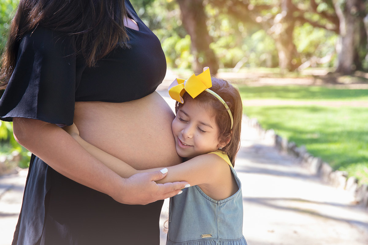 Foto de ensaio de gestante no Jardim Botânico, momento carinhoso com a filha pequena.