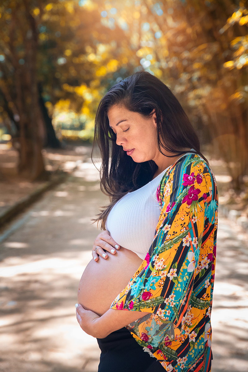 Retrato de gestante em ensaio ao ar livre, rodeada de árvores no Jardim Botânico.