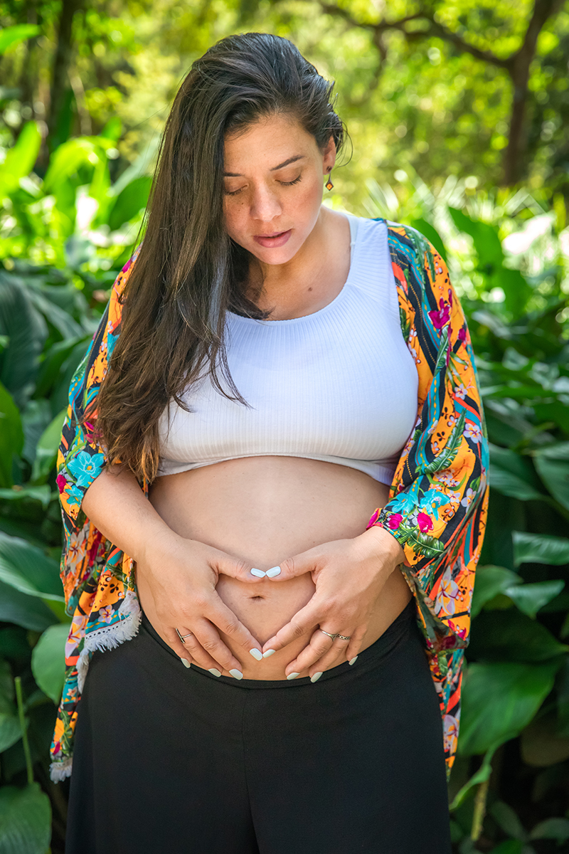 Foto de gestante sorrindo e acariciando a barriga no Jardim Botânico do Rio.