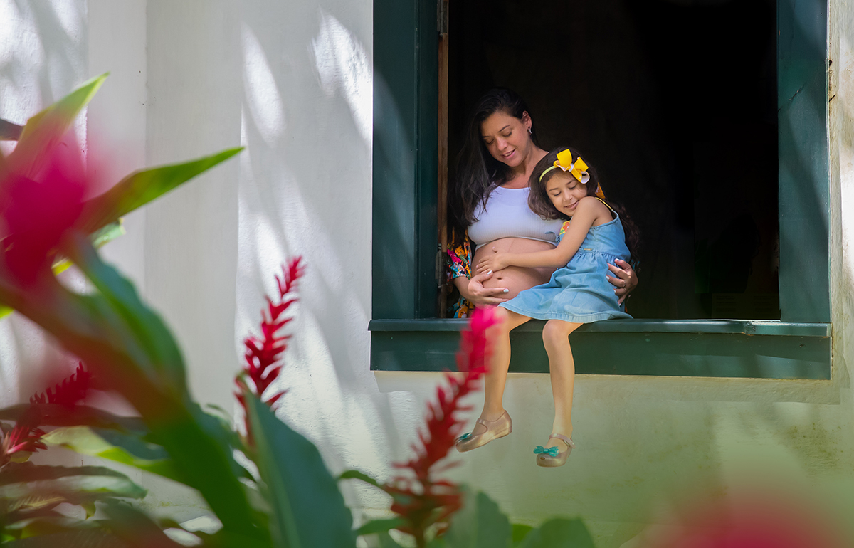 Retrato de gestante e filha sentada  na janela histórica no Jardim Botânico do Rio.