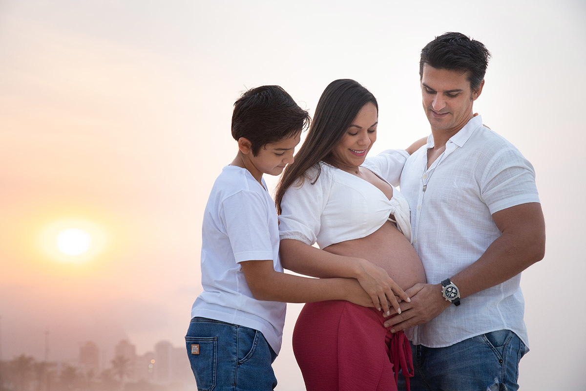 Ensaio de gestante na praia: Silvia, Sanderson e Matheus abraçados, no Rio de Janeiro.