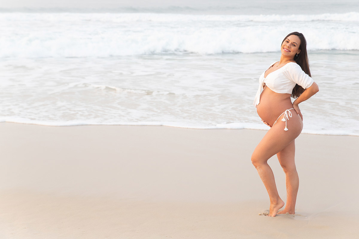 Ensaio de gestante na praia: Silvia em pé em frente ao mar, no Rio de Janeiro.