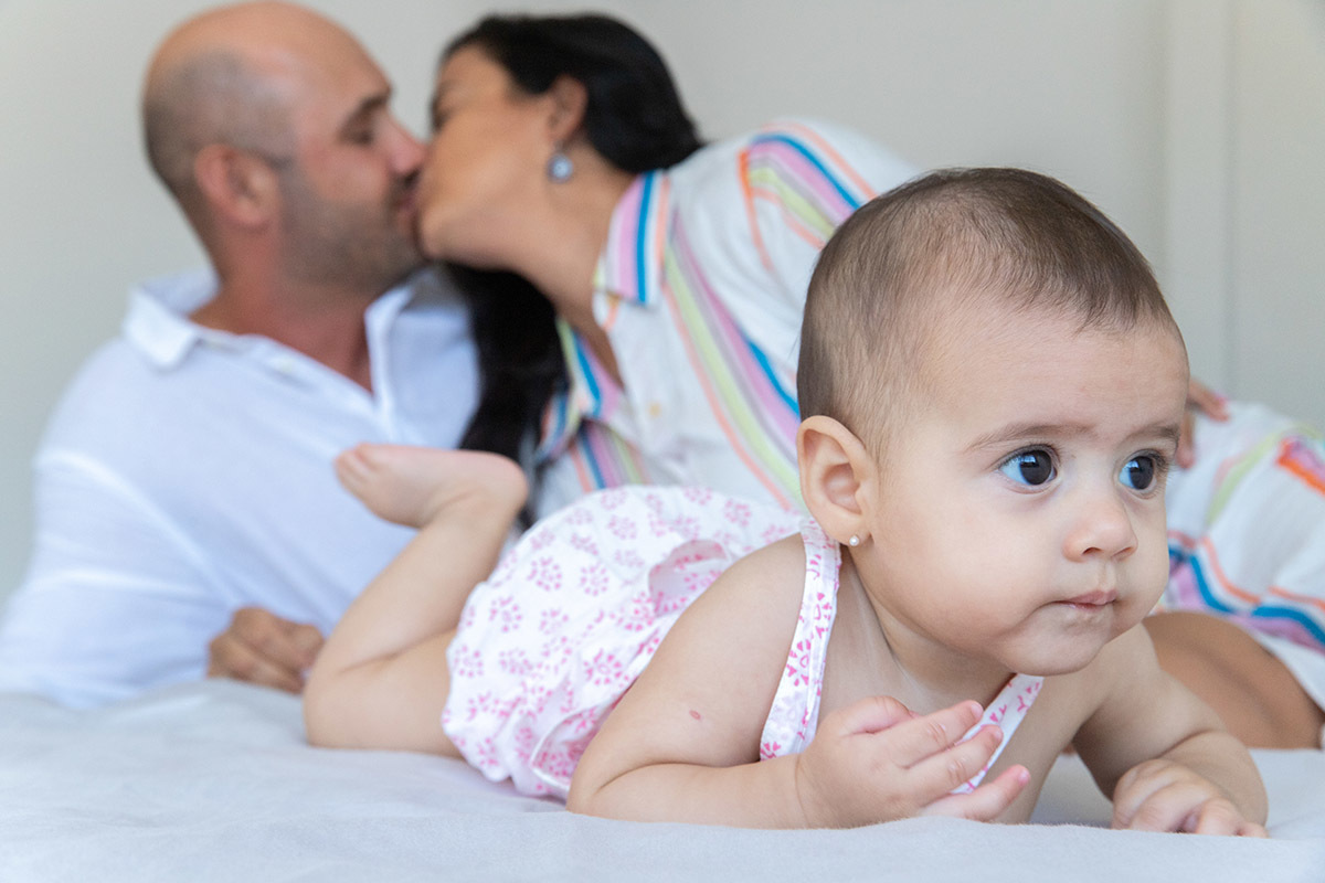 Ensaio de família: Marina deitada na cama com os pai, no Rio de Janeiro.