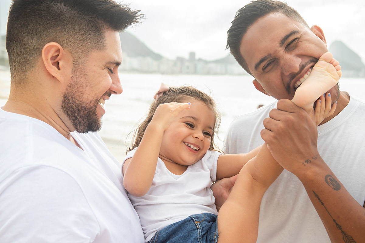 Ensaio família na praia de Copacabana: tio mordendo o pé da sobrinha no Rio de Janeiro.